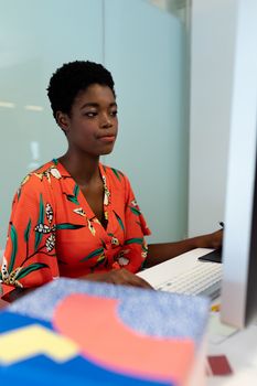 Side view of young pretty African american female graphic designer working on computer at desk in office. This is a casual creative start-up business office for a diverse team