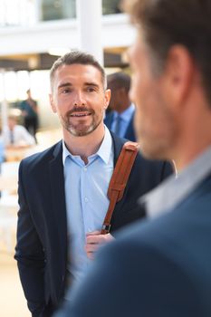 Front view of happy Caucasian businessmen interacting with each other in the corridor at office. International diverse corporate business partnership concept