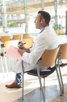 Side view of mature male executive sat in empty conference room thinking while writing on folder