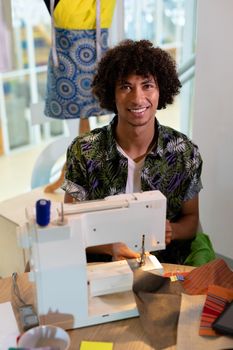 Portrait of mixed race male fashion designer using sewing machine on a table in design studio. This is a casual creative start-up business office for a diverse team