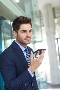 Side view of young Caucasian businessman speaking on mobile phone while standing in modern office