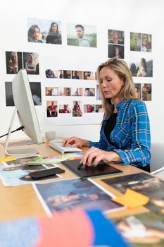 Side view of mature Caucasian female fashion designer using graphic tablet at desk in office. This is a casual creative start-up business office for a diverse team