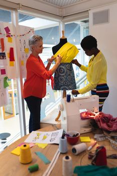 Side view of diverse female graphic designers using measuring tape on a mannequin in design studio. This is a casual creative start-up business office for a diverse team