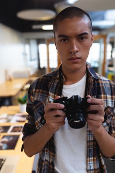 Portrait of mixed race male graphic designer holding a camera in office. This is a casual creative start-up business office for a diverse team