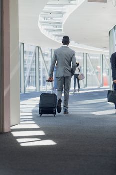 Rear view of African american businessman walking in corridor with suitcase in modern office