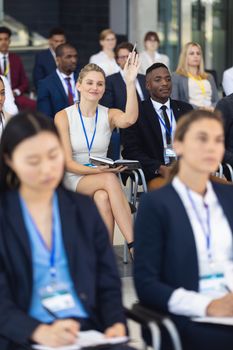 Front view of Young Caucasian businesswoman asking question in speech in conference room. With executives in the background.