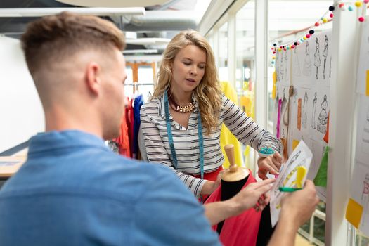 Side view of Caucasian fashion designers discussing over sketch in design studio. This is a casual creative start-up business office for a diverse team