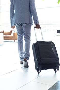 Rear view of young African-american male executive walking with suitcase