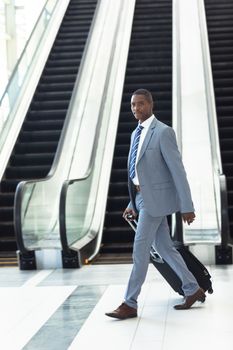 Side view of young African-american executive walking with suitcase in hall