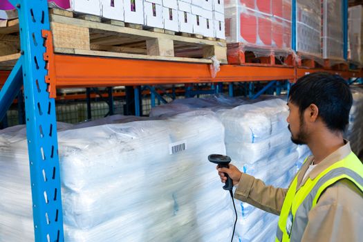 Side view of mature Asian male worker scanning package with barcode scanner in modern warehouse. This is a freight transportation and distribution warehouse. Industrial and industrial workers concept