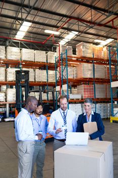 Front view of mature diverse warehouse staff discussing over laptop in warehouse. This is a freight transportation and distribution warehouse. Industrial and industrial workers concept