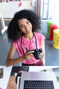Portrait of African american female graphic designer reviewing photos on digital camera at desk in office. This is a casual creative start-up business office for a diverse team