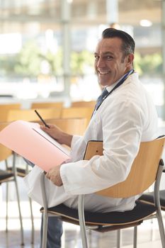 Side view of mature male executive sat in empty conference room smiling at camera