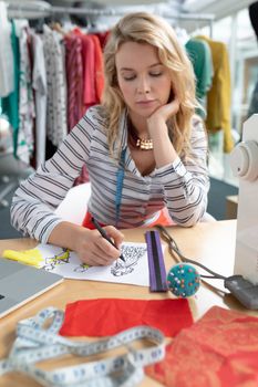 Front view of Caucasian female fashion designer drawing sketch on a table in design studio. This is a casual creative start-up business office for a diverse team