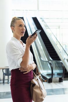 Side view of young Caucasian businesswoman speaking on mobile phone while standing in modern office