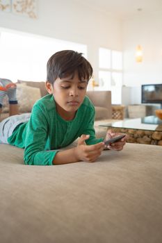 Front view close-up of young cute mixed-race boy playing game on mobile phone while lying on sofa at home