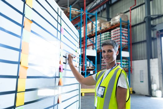 Portrait of beautiful Caucasian female staff writing on whiteboard in warehouse. This is a freight transportation and distribution warehouse. Industrial and industrial workers concept