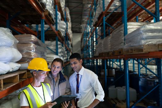 Front view of diverse staffs discussing over digital tablet in warehouse. This is a freight transportation and distribution warehouse. Industrial and industrial workers concept