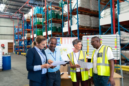 Front view of mature diverse staffs discussing over document in warehouse. This is a freight transportation and distribution warehouse. Industrial and industrial workers concept