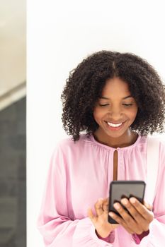 Front view of young pretty African-american employee looking her phone in modern office