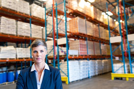 Front view of beautiful mature Caucasian female manager looking at camera in warehouse. This is a freight transportation and distribution warehouse. Industrial and industrial workers concept