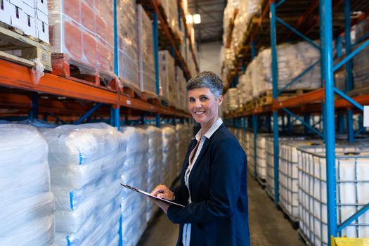 Side view of beautiful mature Caucasian female manager looking at camera while working in warehouse. This is a freight transportation and distribution warehouse. Industrial and industrial workers concept