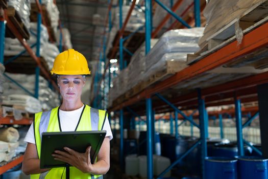 Front view of Caucasian Attentive female staff using digital tablet in warehouse. This is a freight transportation and distribution warehouse. Industrial and industrial workers concept