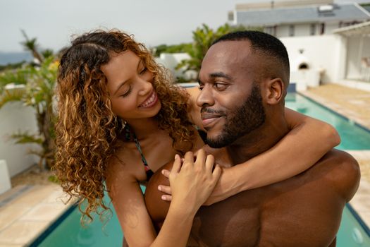 Close-up of African-american man giving piggyback ride to woman near swimming pool at the backyard of home. Summer fun at home by the swimming pool