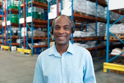 Portrait close up of happy African-american male supervisor with headset looking at camera in warehouse. This is a freight transportation and distribution warehouse. Industrial and industrial workers concept