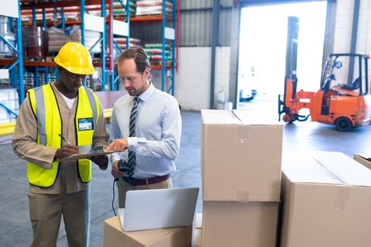 Front view of diverse staffs discussing over clipboard in warehouse. This is a freight transportation and distribution warehouse. Industrial and industrial workers concept
