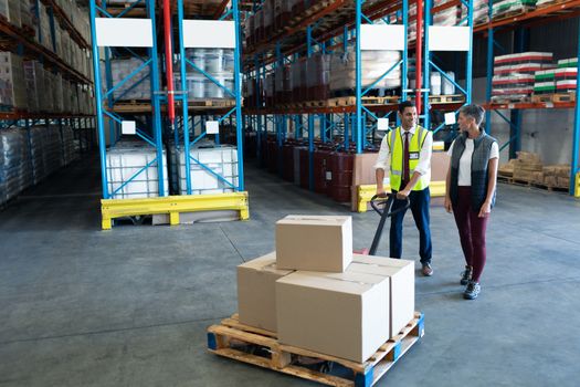 Front view of Caucasian Male staff with his Caucasian female coworker using pallet jack in warehouse. This is a freight transportation and distribution warehouse. Industrial and industrial workers concept