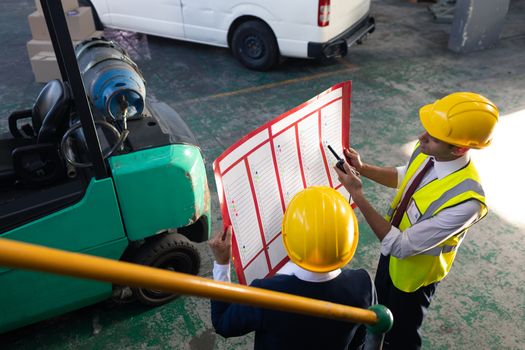 High angle view of Caucasian female manager and Caucasian male supervisor discussing over inventory chart in warehouse. This is a freight transportation and distribution warehouse. Industrial and industrial workers concept