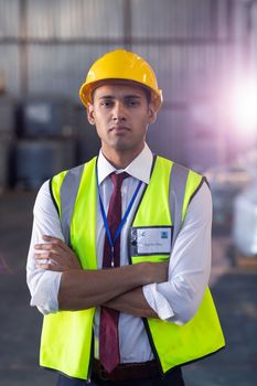 Close-up of African-american male staff in hardhat and reflective jacket standing with arms crossed in warehouse. This is a freight transportation and distribution warehouse. Industrial and industrial workers concept