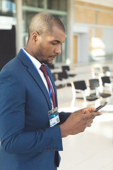 Side view of young African-american male executive standing in empty conference room, texting on mobile phone