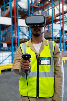 Front view of handsome mature Asian male worker with barcode scanner using virtual reality headset in warehouse. This is a freight transportation and distribution warehouse. Industrial and industrial workers concept