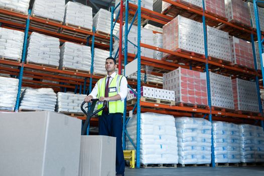 Low angle view of Caucasian male staff using pallet jack in warehouse. This is a freight transportation and distribution warehouse. Industrial and industrial workers concept
