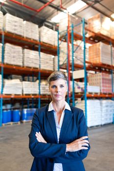 Portrait close-up of beautiful mature Caucasian female manager standing with arm crossed and looking at camera in warehouse. This is a freight transportation and distribution warehouse. Industrial and industrial workers concept