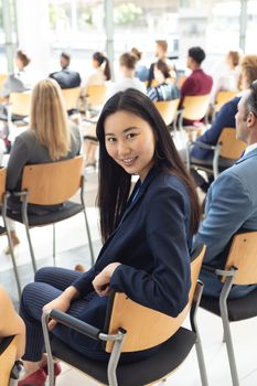 Side view of young Asian businesswoman sat in conference room, smiling to camera