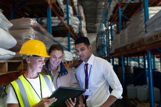 Front view of diverse staffs discussing over digital tablet in warehouse. This is a freight transportation and distribution warehouse. Industrial and industrial workers concept