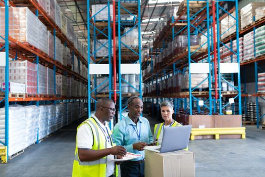 Front view of mature diverse warehouse staffs discussing over laptop in warehouse. This is a freight transportation and distribution warehouse. Industrial and industrial workers concept
