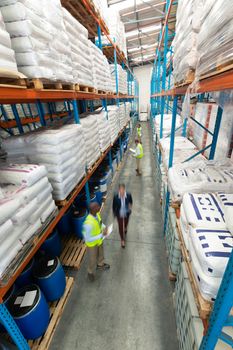 High angle view of diverse warehouse staff checking stocks in aisle in warehouse. They are holding clipboards and writing in it. This is a freight transportation and distribution warehouse. Industrial and industrial workers concept