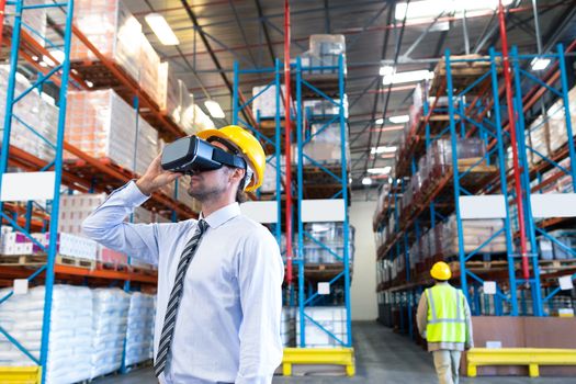 Front view of handsome Caucasian male supervisor using virtual reality headset in warehouse. This is a freight transportation and distribution warehouse. Industrial and industrial workers concept