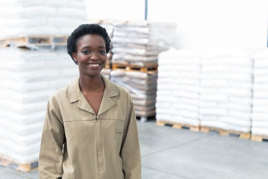Portrait of happy pretty African-american female worker looking at camera in warehouse. This is a freight transportation and distribution warehouse. Industrial and industrial workers concept