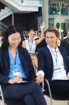 Front view of Young Caucasian businesswoman asking question in speech in conference room. With executives in the background.