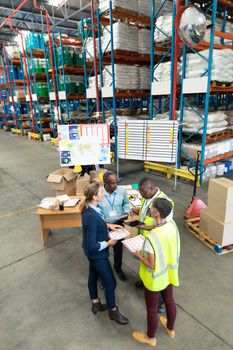 High angle view of mature diverse staffs discussing over document in warehouse. This is a freight transportation and distribution warehouse. Industrial and industrial workers concept