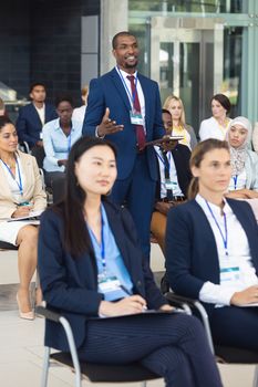 Front view of African american businessman standing while listening to speech in conference room