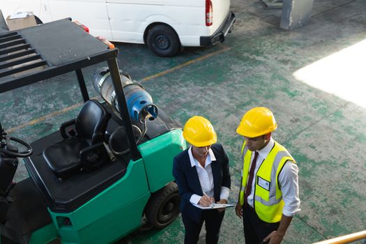 High angle view of Caucasian female manager and male supervisor discussing over clipboard in warehouse. This is a freight transportation and distribution warehouse. Industrial and industrial workers concept