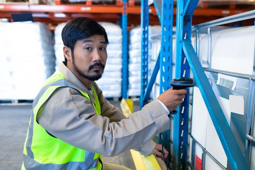 Side view of mature Asian male worker looking at camera while scanning package in modern warehouse. This is a freight transportation and distribution warehouse. Industrial and industrial workers concept