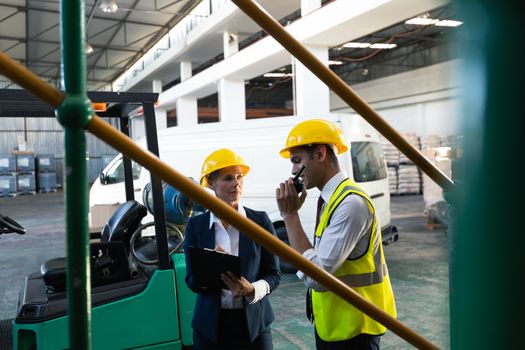 Front view of Caucasian female manager and Caucasian male supervisor working together in warehouse. This is a freight transportation and distribution warehouse. Industrial and industrial workers concept