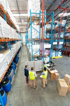 High angle view of mature diverse warehouse staff discussing over whiteboard in warehouse. This is a freight transportation and distribution warehouse. Industrial and industrial workers concept